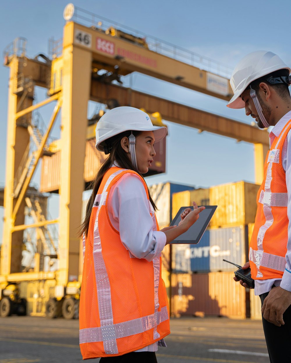 Two Smarttcargo coordinators in hi-vis checking a shipment on a tablet in a container yard